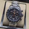 TAG Heuer — esfera negra con detalles naranjas y brazalete plateado