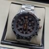 TAG Heuer — esfera negra con detalles naranjas y brazalete plateado