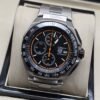 TAG Heuer — esfera negra con detalles naranjas y brazalete plateado