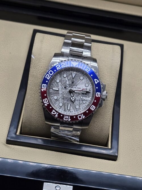 Rolex — esfera gris texturizada con bisel rojo y azul, brazalete plateado