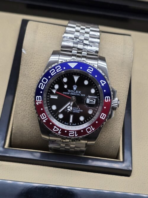 Rolex — esfera oscura con bisel rojo y azul, brazalete plateado