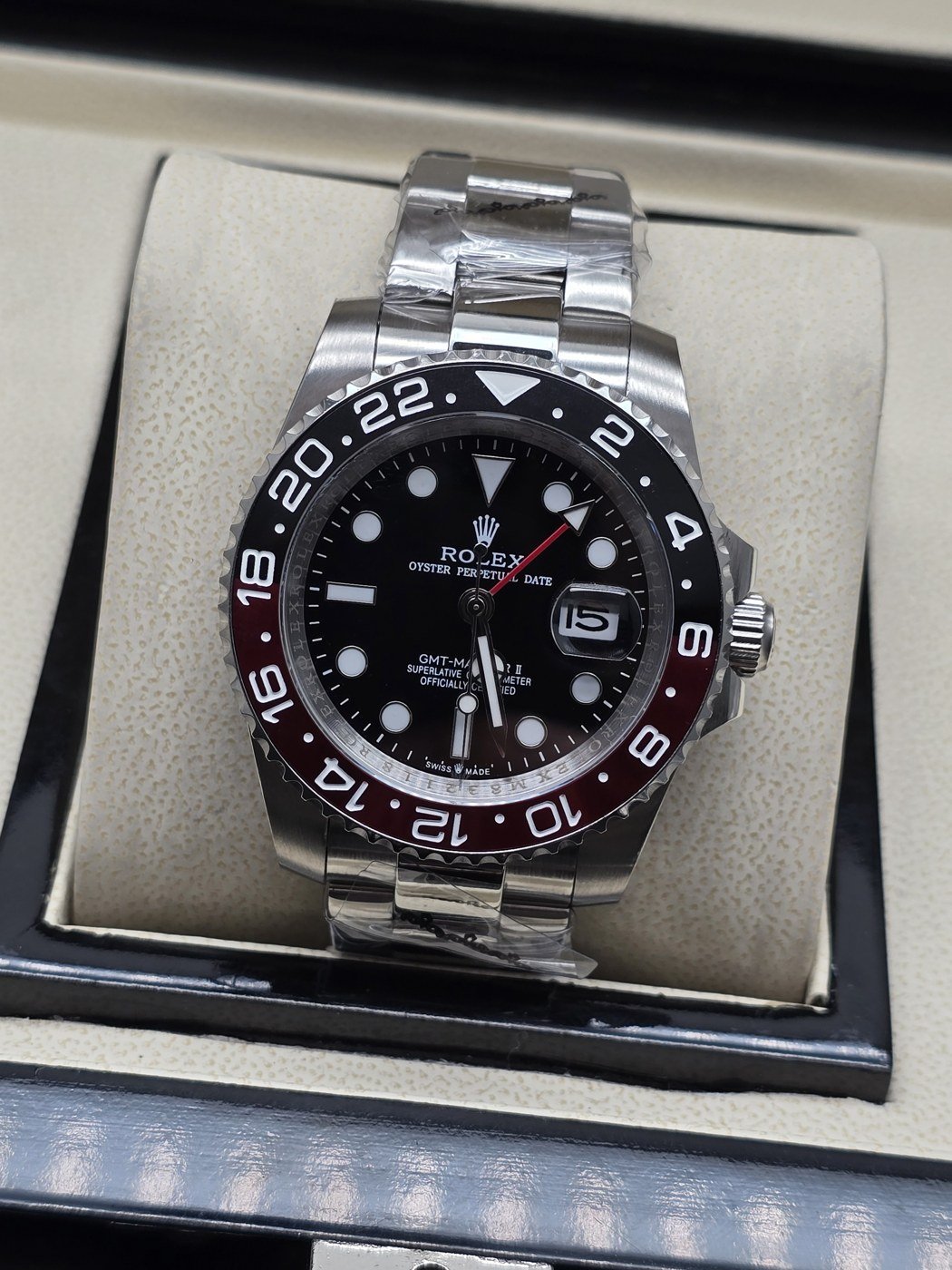 Rolex — esfera negra con bisel oscuro y rojo, brazalete plateado