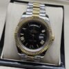 Rolex — esfera negra con números romanos y bisel dorado y brazalete bicolor · 41 mm