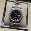 Rolex — esfera negra con bisel rosado estriado y brazalete bicolor · 36 mm