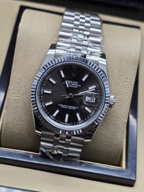 Rolex — esfera negra con números romanos y bisel estriado y brazalete plateado · 36 mm