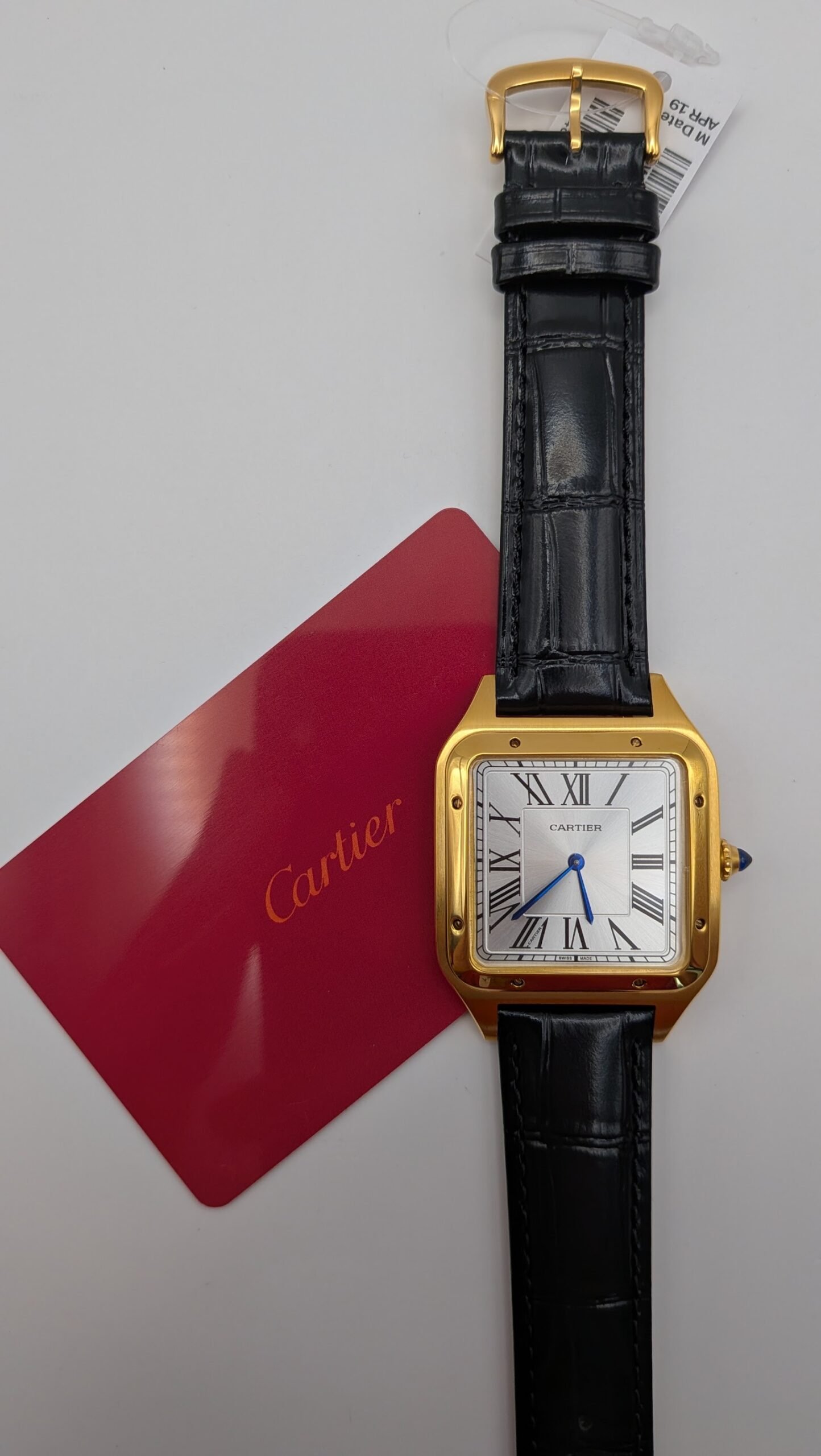 Cartier — caja rectangular dorada, esfera blanca con números romanos y correa de cuero negra