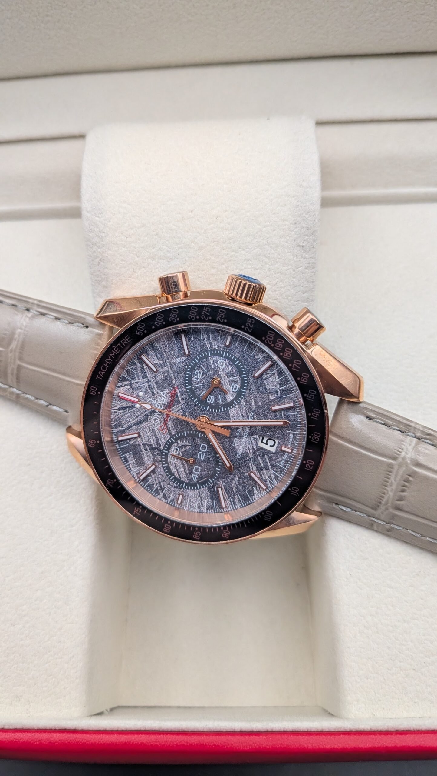 Omega — cronógrafo con esfera gris texturizada, caja oro rosa y correa de cuero gris
