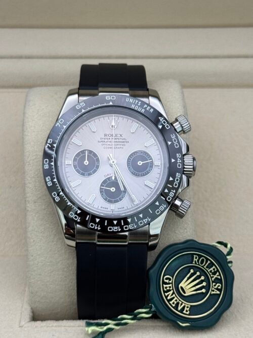 Rolex — cronógrafo con esfera plateada y subesferas negras, bisel negro y correa de caucho negra