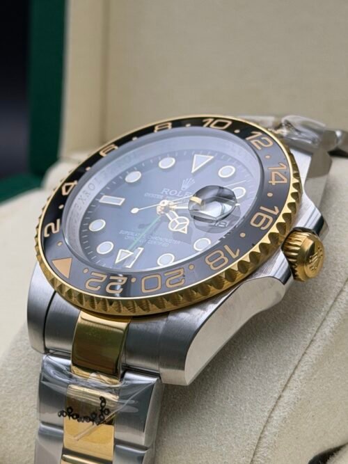 Rolex — esfera negra con doble huso horario, bisel dorado y negro y brazalete bicolor