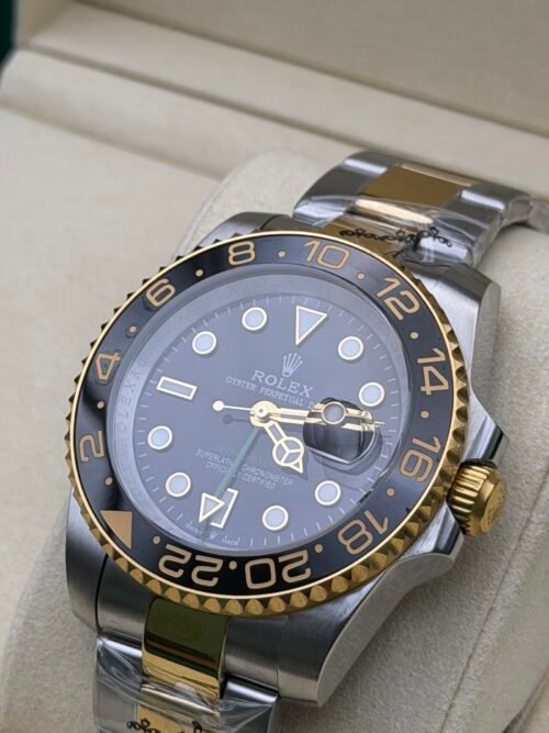 Rolex — esfera negra con doble huso horario, bisel dorado y negro y brazalete bicolor