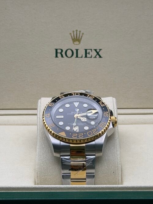 Rolex — esfera negra con doble huso horario, bisel dorado y negro y brazalete bicolor