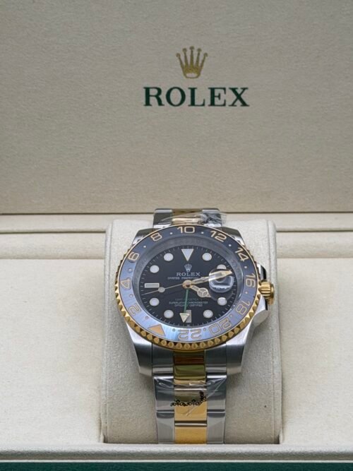Rolex — esfera negra con doble huso horario, bisel gris y dorado y brazalete bicolor