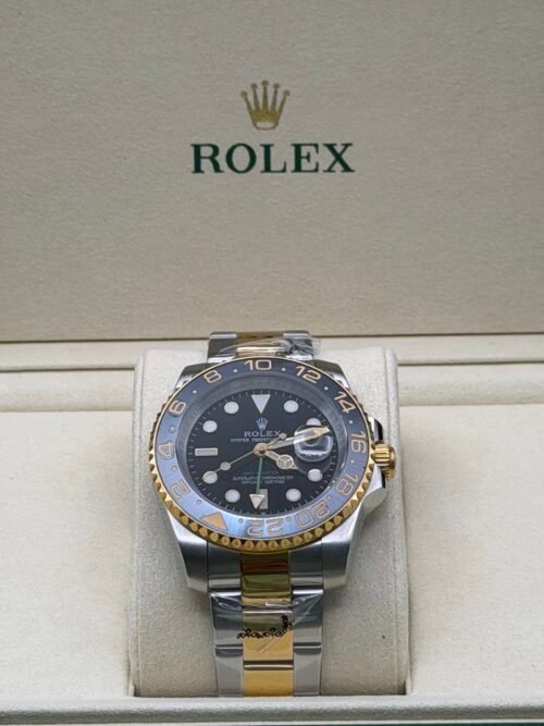 Rolex — esfera negra con doble huso horario, bisel gris y dorado y brazalete bicolor