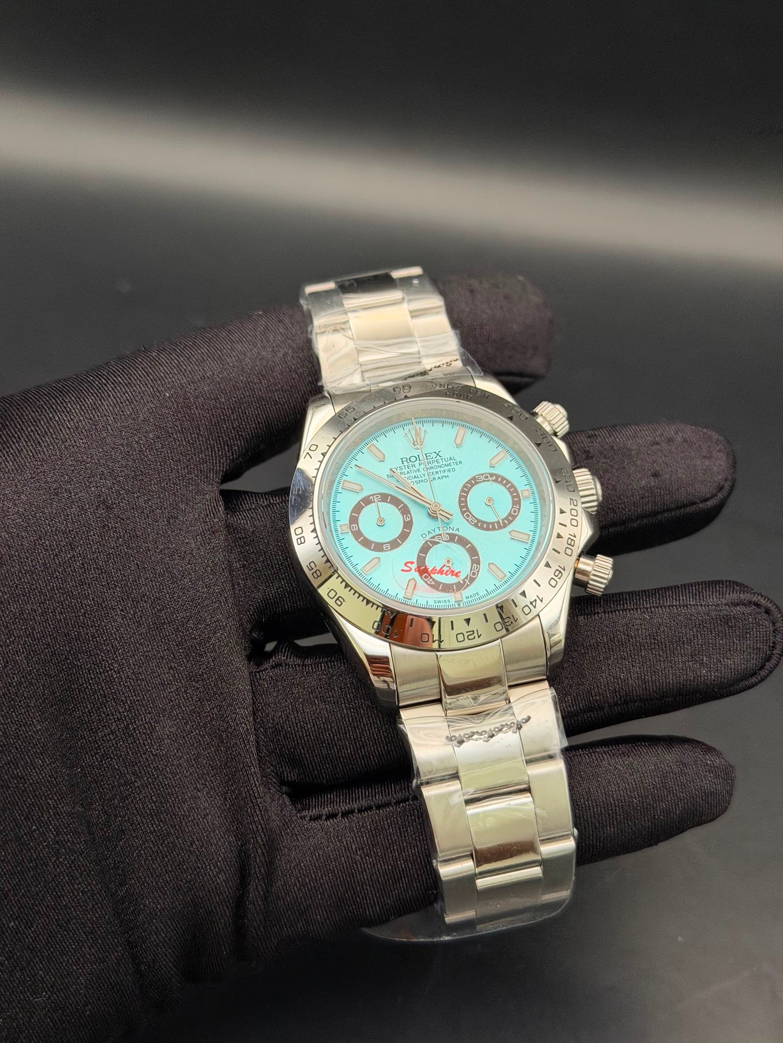 Rolex — cronógrafo con esfera turquesa y detalles rojos, brazalete de acero