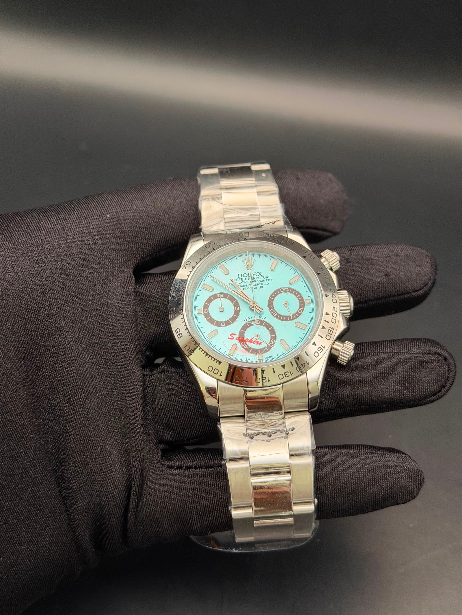 Rolex — cronógrafo con esfera turquesa y detalles rojos, brazalete de acero