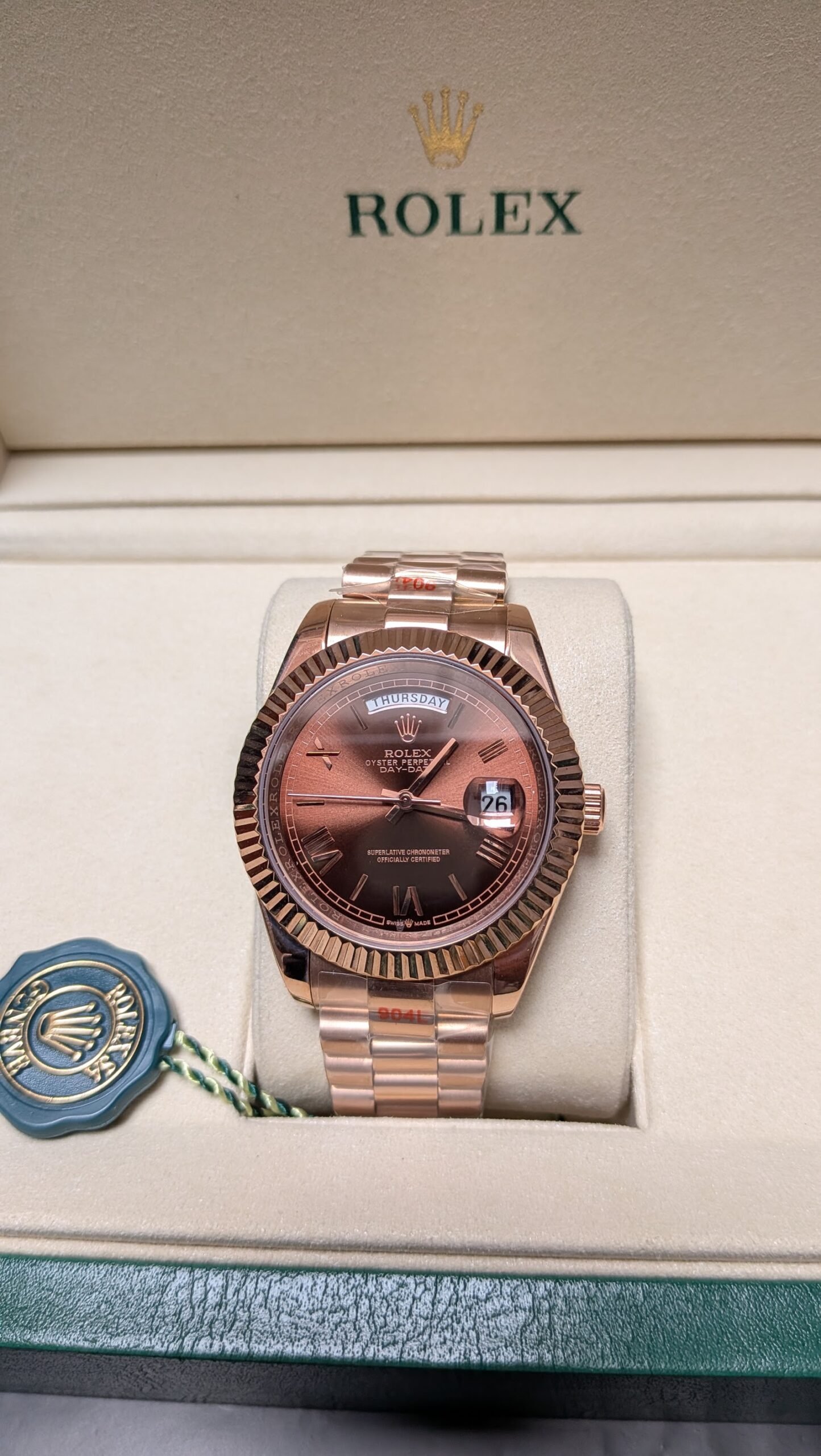 Rolex — esfera chocolate con día y fecha, bisel estriado y brazalete oro rosa
