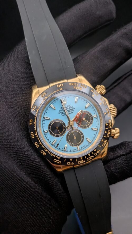 Rolex — cronógrafo con esfera turquesa y subesferas marrones, caja dorada y correa de caucho gris
