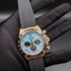 Rolex — cronógrafo con esfera turquesa y subesferas marrones, caja dorada y correa de caucho gris