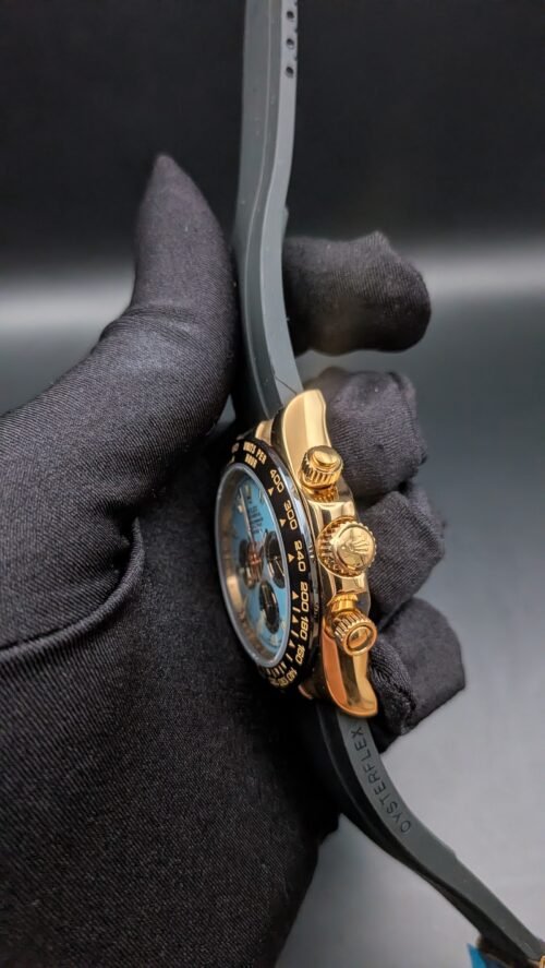 Rolex — cronógrafo con esfera turquesa y subesferas marrones, caja dorada y correa de caucho gris