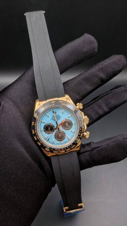 Rolex — cronógrafo con esfera turquesa y subesferas marrones, caja dorada y correa de caucho gris