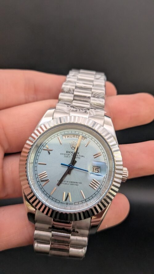 Rolex — esfera azul hielo con números romanos, día y fecha, bisel estriado y brazalete de acero