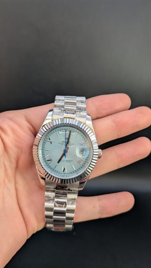 Rolex — esfera azul hielo con números romanos, día y fecha, bisel estriado y brazalete de acero