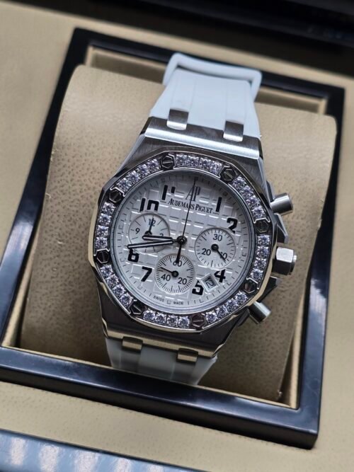 Audemars Piguet — cronógrafo con esfera blanca y números negros, bisel con brillantes y correa gris clara
