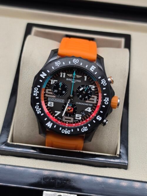 Breitling — cronógrafo negro con aro rojo y azul y correa naranja