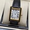 Cartier — caja rectangular dorada, esfera blanca con números romanos y correa de cuero negra
