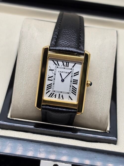 Cartier — caja rectangular dorada, esfera blanca con números romanos y correa de cuero negra