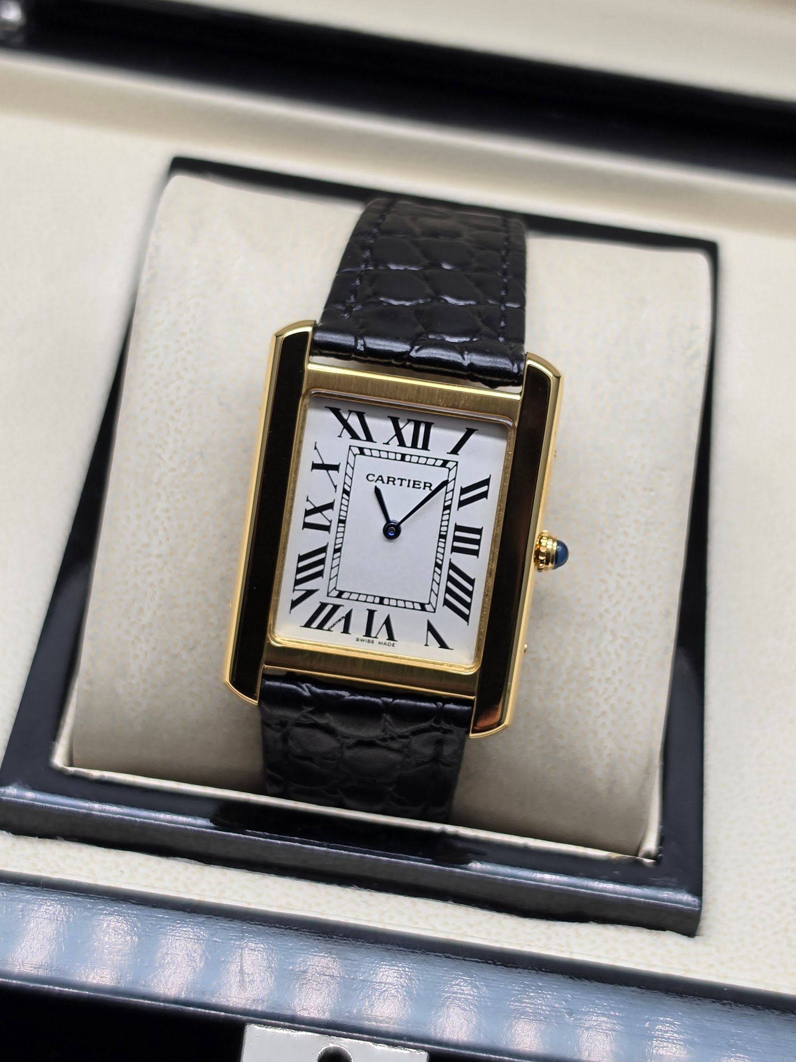 Cartier — caja rectangular dorada, esfera blanca con números romanos y correa negra texturizada
