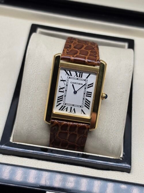 Cartier — caja rectangular dorada, esfera blanca con números romanos y correa de cuero marrón