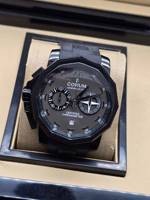 Corum — cronógrafo con esfera gris, caja negra y correa de caucho negra