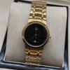 Movado — esfera negra minimalista, caja dorada y brazalete dorado