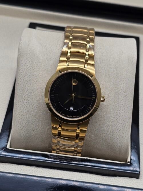 Movado — esfera negra minimalista, caja dorada y brazalete dorado