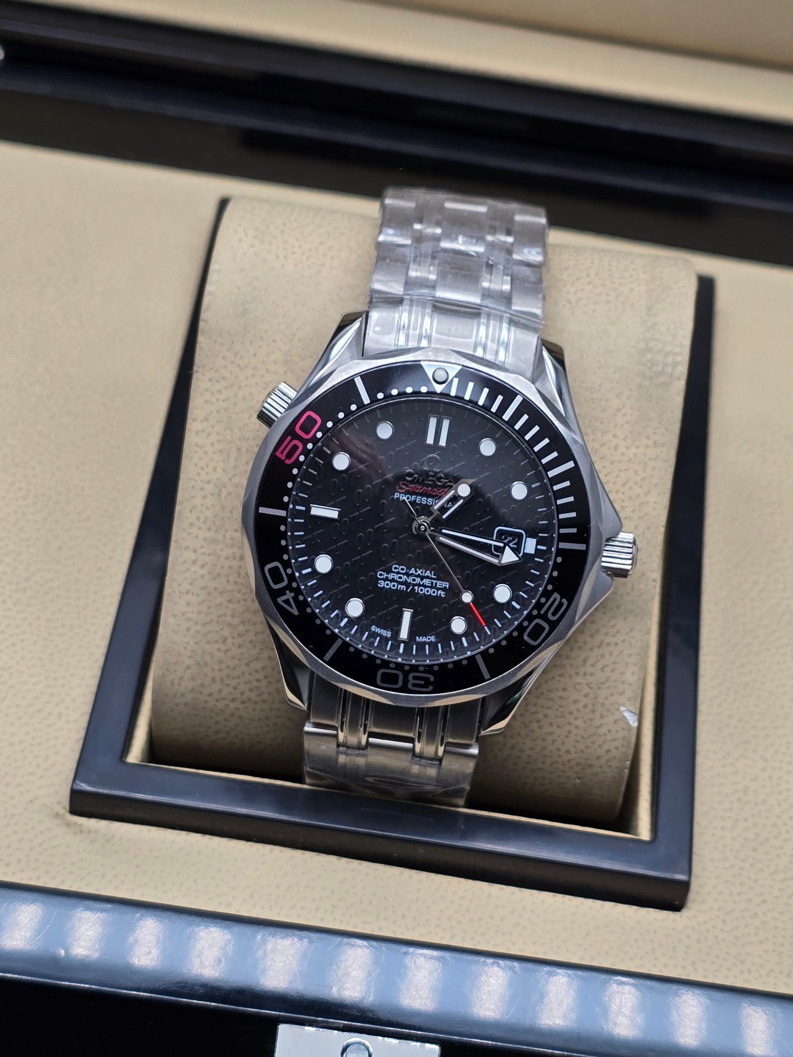 Omega — esfera negra con detalles rojos, bisel negro y brazalete de acero