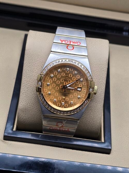 Omega — esfera dorada texturizada, bisel con brillantes y brazalete bicolor