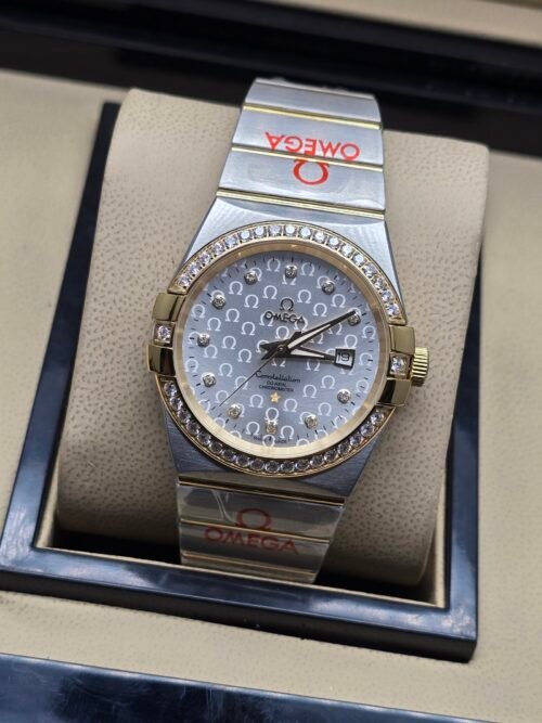 Omega — esfera plateada texturizada, bisel dorado con brillantes y brazalete bicolor