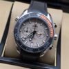 Omega — cronógrafo con esfera gris clara, bisel negro con detalle naranja y correa negra