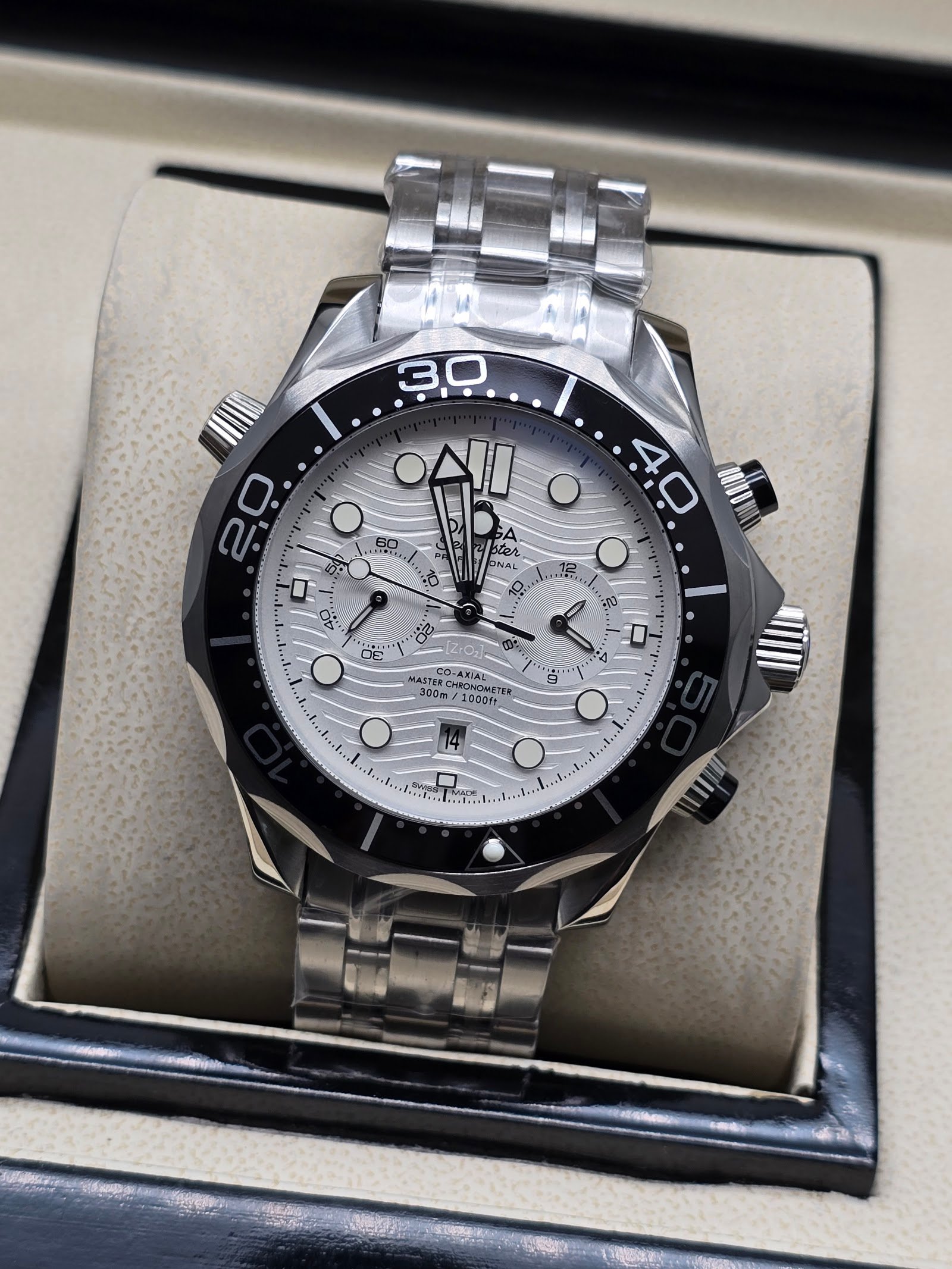 Omega — cronógrafo con esfera blanca ondulada, bisel negro y brazalete de acero