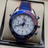 Omega — cronógrafo con esfera blanca, bisel azul con detalle naranja y correa de tela azul