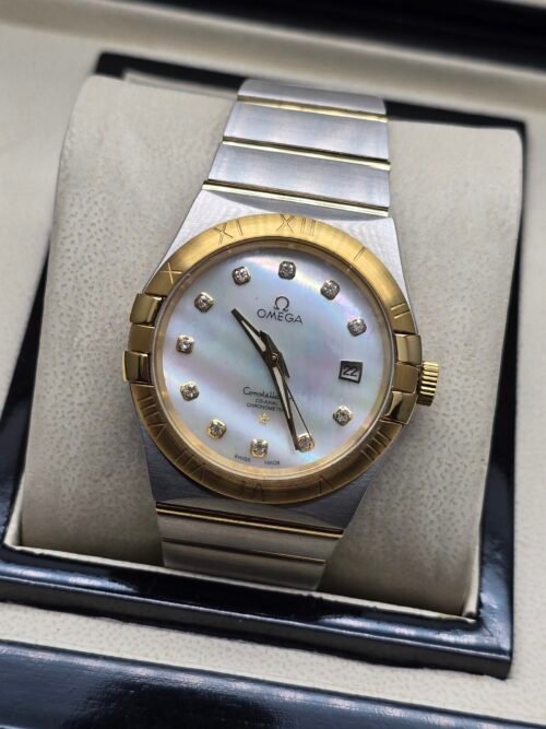 Omega — esfera blanca nacarada, bisel dorado y brazalete bicolor