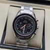 Omega — cronógrafo con esfera negra y detalles naranjas, brazalete de acero