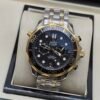Omega — cronógrafo con esfera negra ondulada, bisel dorado y brazalete bicolor