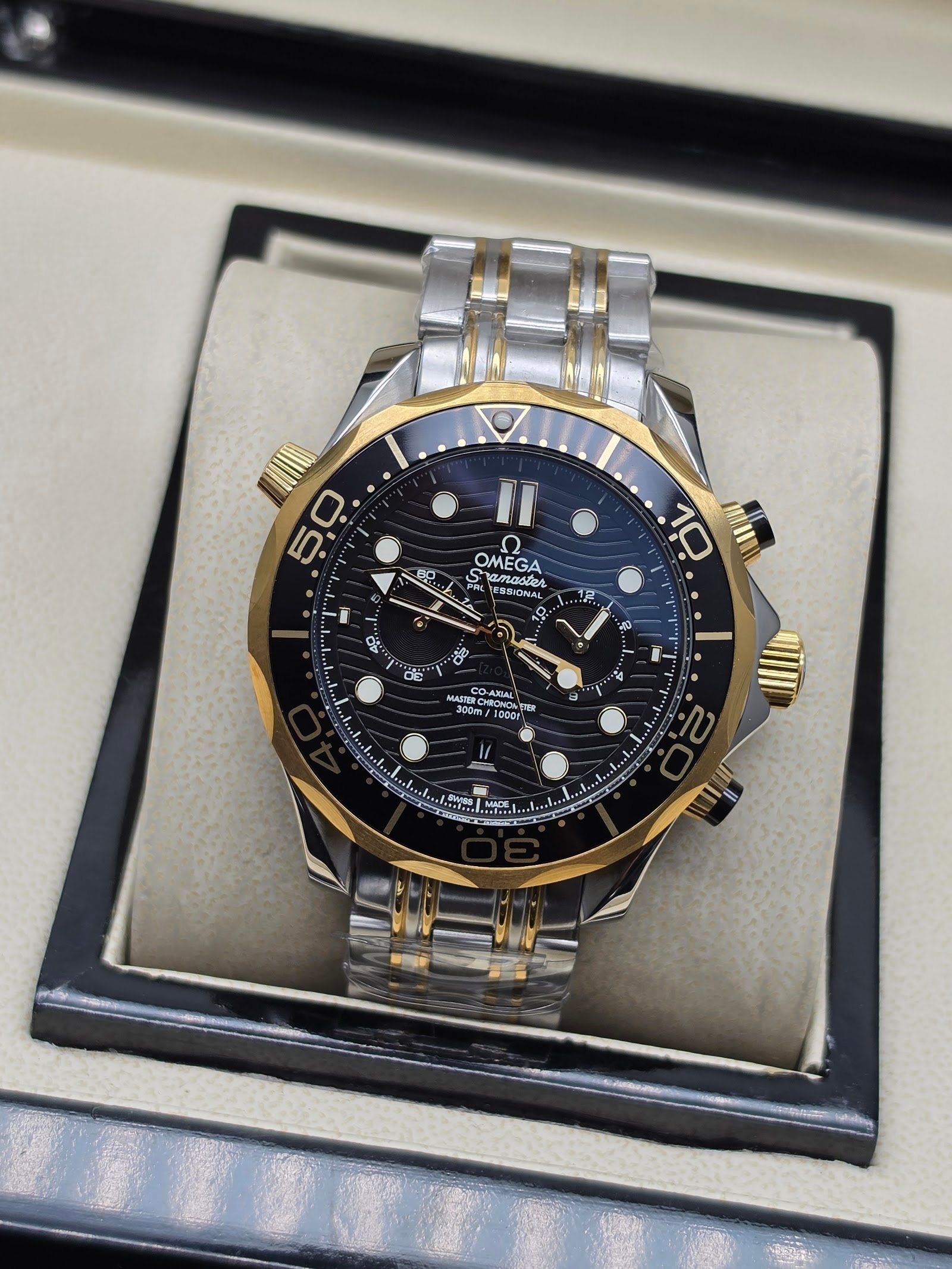 Omega — cronógrafo con esfera negra ondulada, bisel dorado y brazalete bicolor