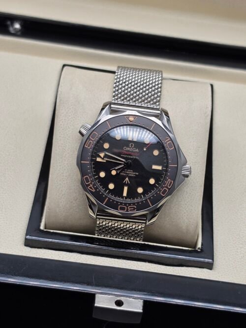 Omega — esfera negra con detalles beige, bisel marrón y brazalete de malla de acero