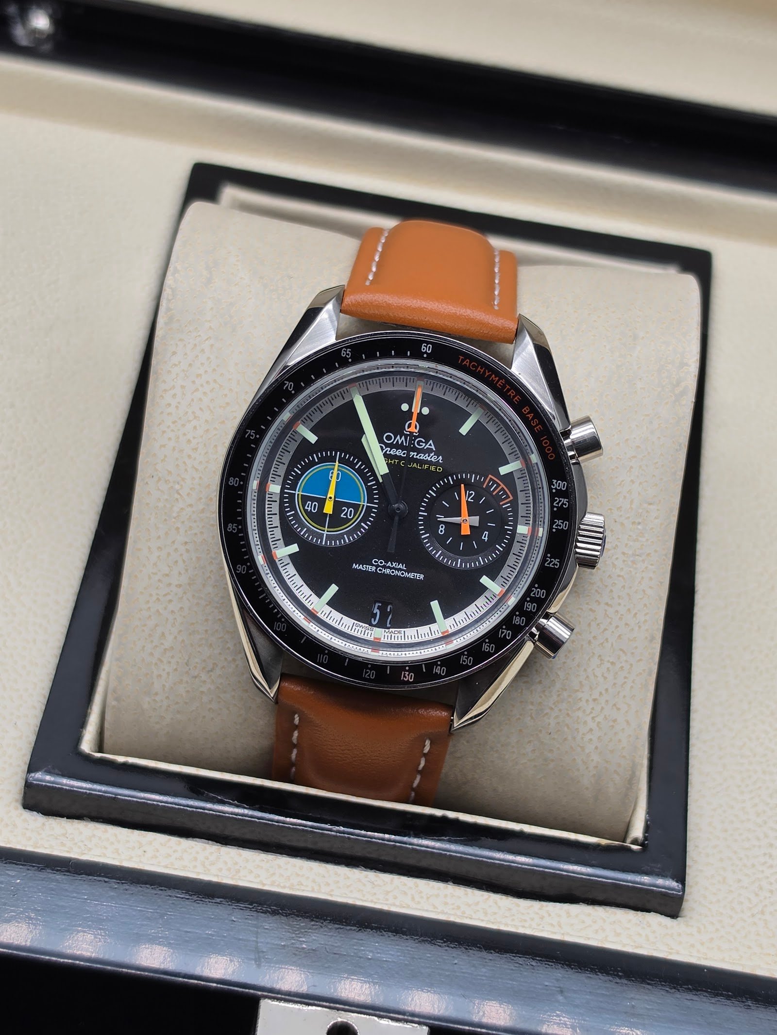 Omega — cronógrafo con esfera negra y agujas de colores, correa de cuero marrón claro