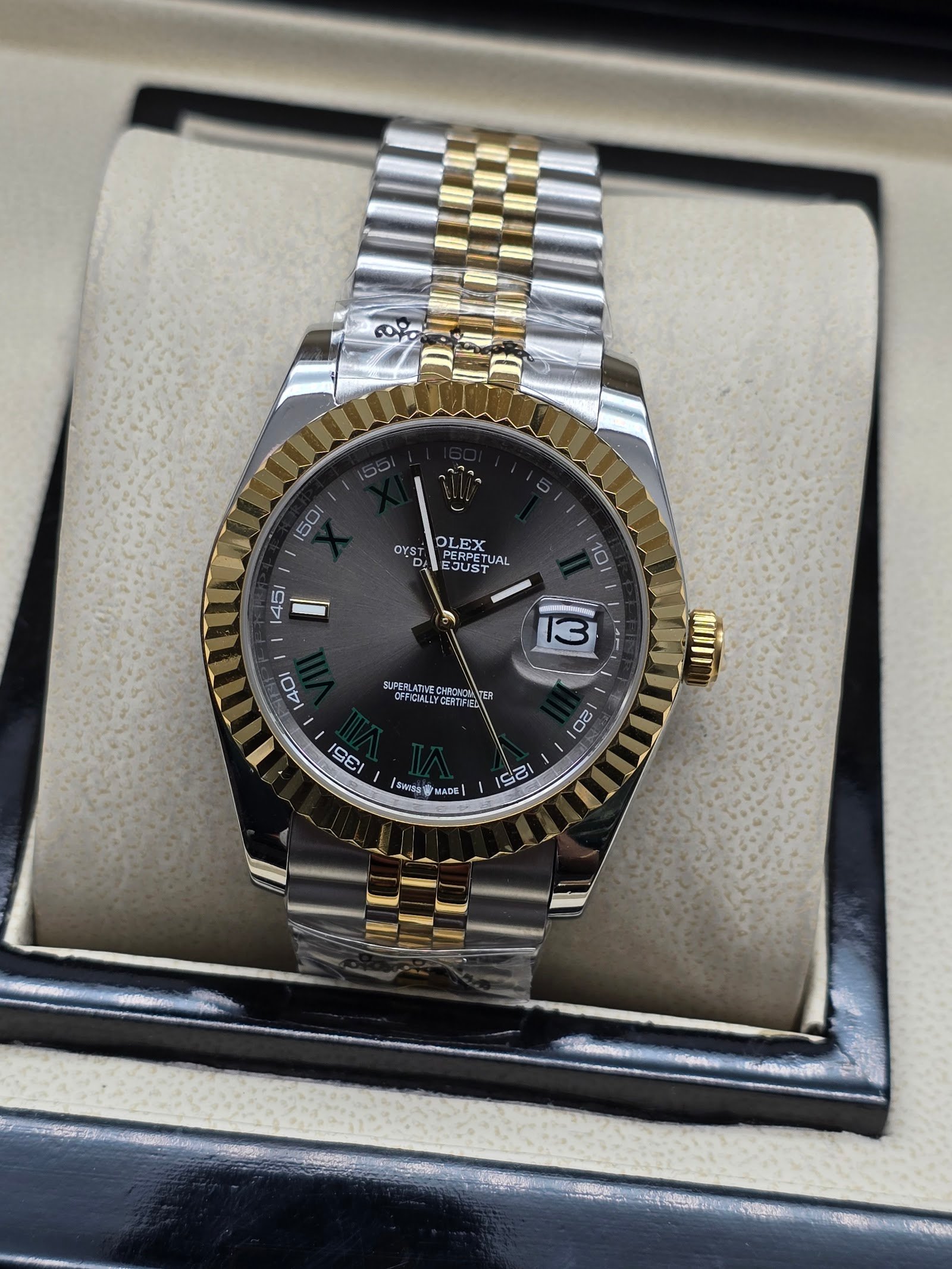 Rolex — esfera gris con números romanos verdes, bisel dorado y brazalete jubilee bicolor