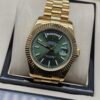 Rolex — esfera verde con día y fecha, bisel dorado estriado y brazalete dorado