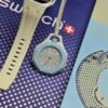 Swatch — reloj de bolsillo octagonal celeste con esfera clara y correa beige